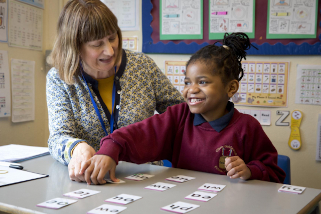 child and teacher at at school desk, looking at letter cards