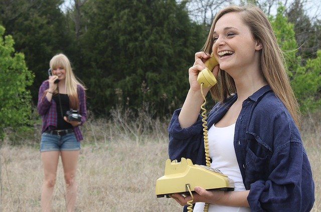 two women stood apart in a field, talking on rotary phones and smiling