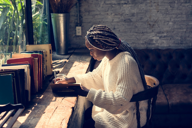 writer sat by a window, surrounded by books and plants