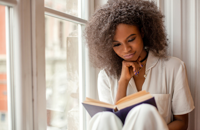 woman reading a book sat on a windowsill