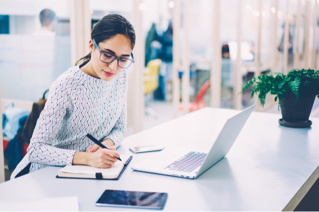 woman works on a laptop, writes in a notebook